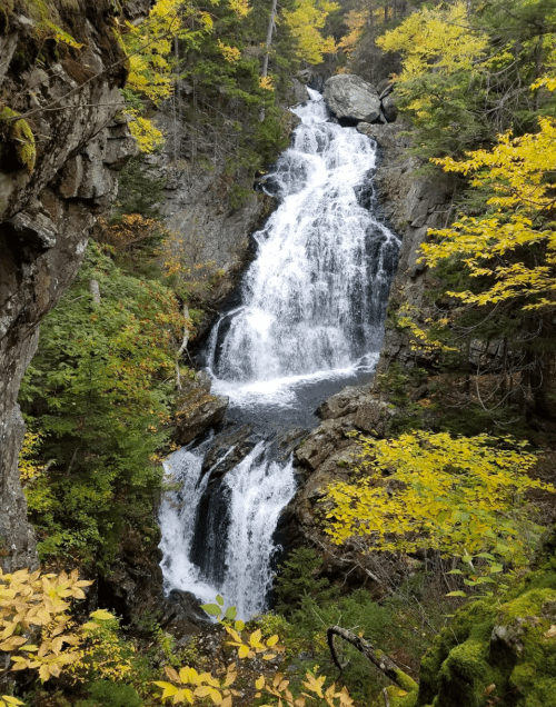 A cascading waterfall surrounded by vibrant autumn foliage and rocky cliffs.