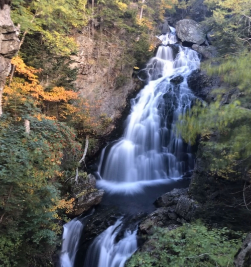 A cascading waterfall surrounded by vibrant autumn foliage and rocky cliffs.