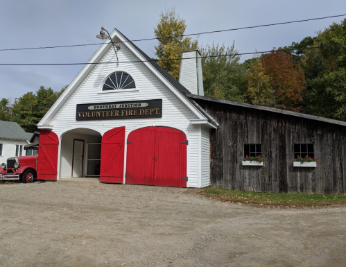 A quaint fire department building with red doors, surrounded by trees in autumn colors.