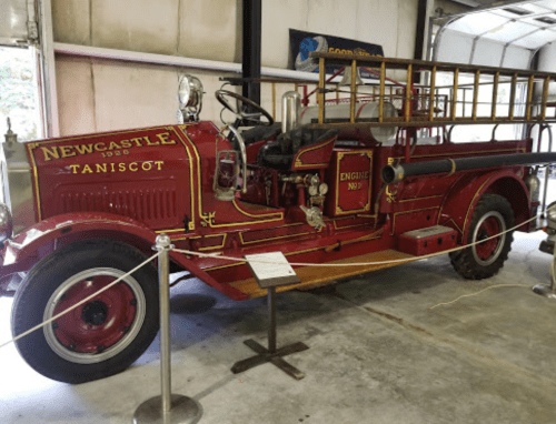A vintage red fire truck from 1920, displayed indoors with a wooden ladder and engine details visible.