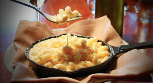 A fork lifts cheesy macaroni from a cast iron skillet, resting on a cloth napkin.