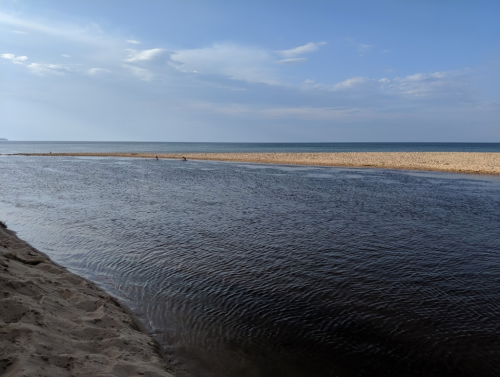 A serene beach scene with a calm river flowing into the ocean under a clear blue sky.