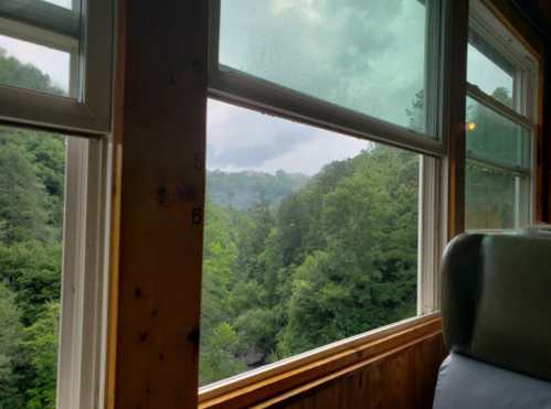 View from a train window showing lush green mountains and cloudy skies in the distance.