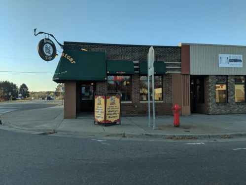 A brick building with green awnings, featuring a sign for a restaurant and a colorful sandwich board outside.