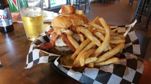 A hearty burger topped with bacon and cheese, served with a generous portion of fries and a glass of beer.