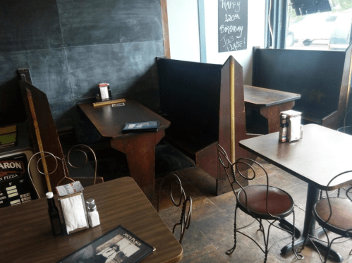 Cozy restaurant interior with wooden booths and tables, chalkboard wall, and menus on the tables.