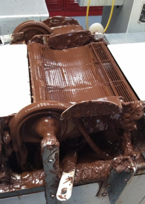 A chocolate mixing machine with thick, melted chocolate coating the interior and spilling over the edges.