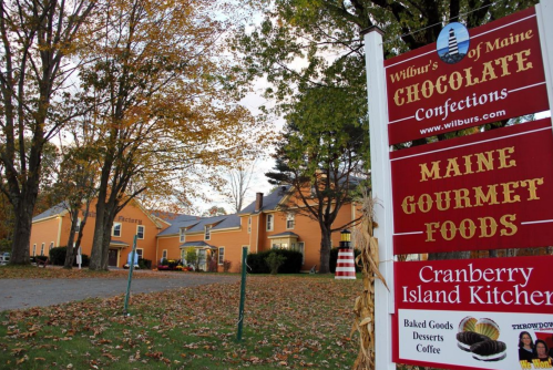 A sign for Wilbur's of Maine Chocolate Confections and Maine Gourmet Foods, surrounded by autumn foliage.