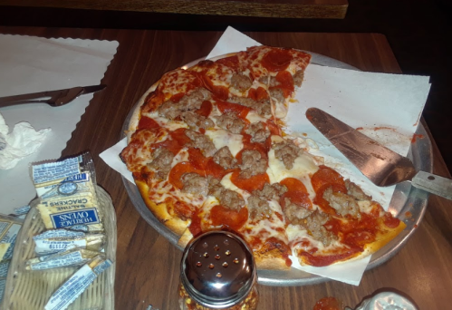 A pizza topped with pepperoni and sausage, served on a metal tray with condiments and a pizza cutter nearby.
