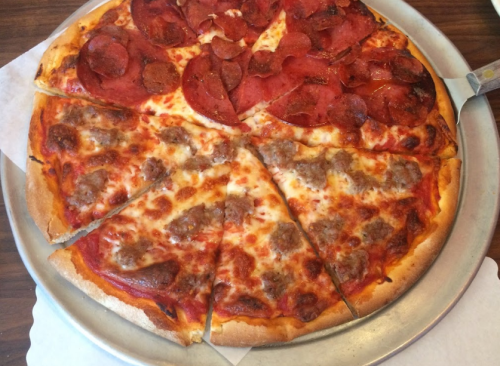 A pizza divided into slices, topped with pepperoni and sausage on a golden crust, served on a metal tray.