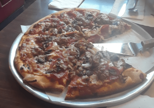 A large pizza topped with pepperoni, sausage, mushrooms, and onions, served on a metal tray with a pizza cutter.