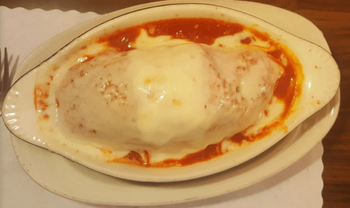 A baked dish with a large stuffed pasta covered in marinara sauce and melted cheese, served in a white oval dish.