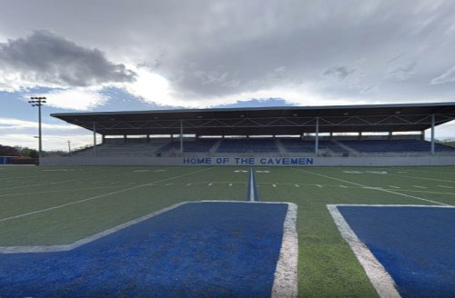 A sports field with a grandstand labeled "HOME OF THE CAVEMEN" under a cloudy sky.