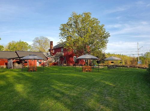 A red barn-style building with outdoor seating under canopies on a grassy lawn, surrounded by trees and blue sky.