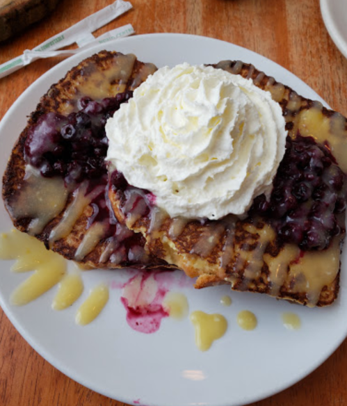 A plate of French toast topped with blueberry sauce and whipped cream, drizzled with a sweet glaze.