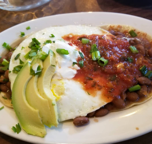A plate of huevos rancheros featuring eggs, beans, avocado, sour cream, and salsa, garnished with green onions.