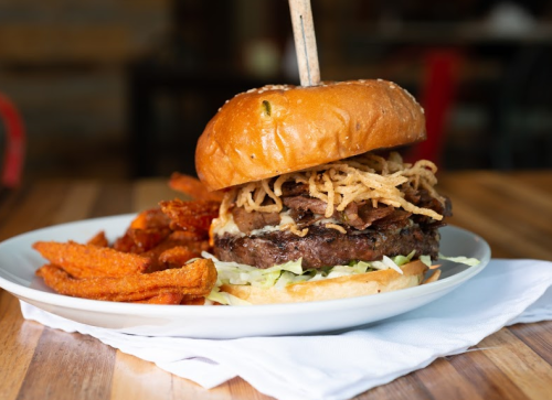 A juicy burger topped with crispy onions on a plate with sweet potato fries.