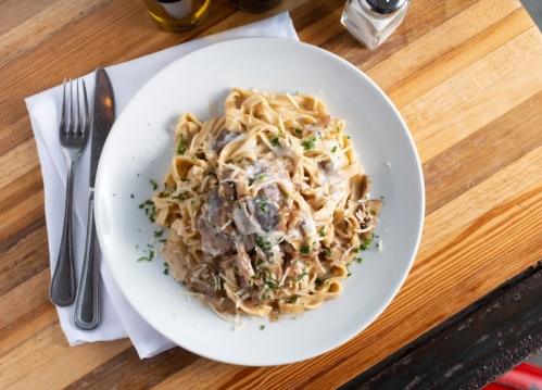 A plate of fettuccine pasta topped with creamy sauce, herbs, and grated cheese, served on a wooden table.