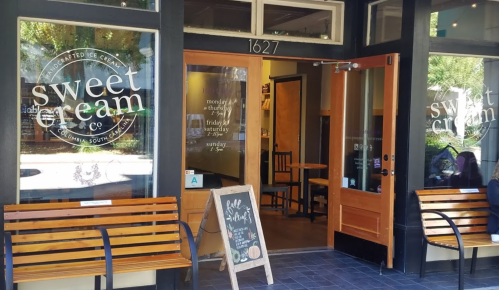 Exterior of Sweet Cream Co. ice cream shop, featuring wooden benches and a chalkboard sign outside.