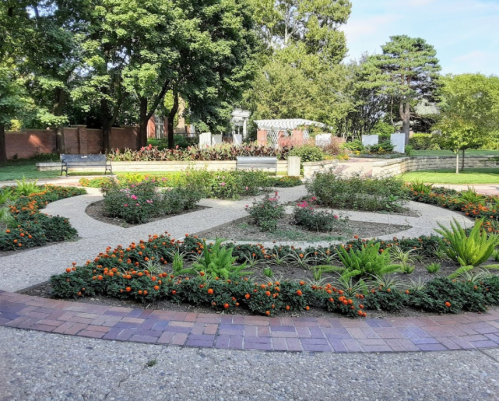 A landscaped garden with winding paths, colorful flowers, and greenery under a clear blue sky.