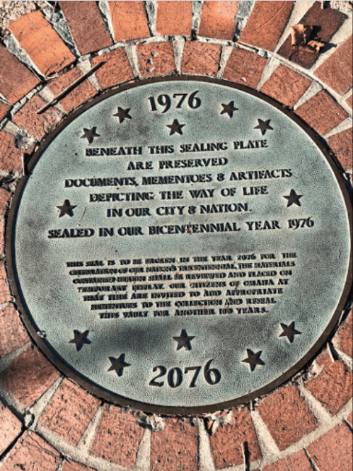Bronze plaque commemorating the years 1976 and 2076, detailing preserved documents and artifacts of local history.