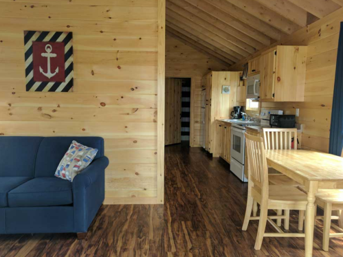 Cozy wooden interior of a cabin featuring a sofa, dining table, and kitchen with nautical decor.