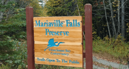 Wooden sign for Mariaville Falls Preserve, indicating trails are open to the public, surrounded by trees.