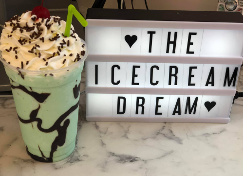 A mint chocolate milkshake topped with whipped cream, sprinkles, and a cherry, next to a sign that reads "THE ICECREAM DREAM."