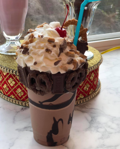 A decadent chocolate milkshake topped with whipped cream, a cherry, and crushed cookies, served in a chocolate-coated cup.