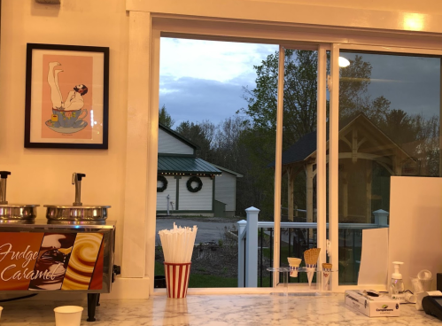A cozy ice cream shop interior with a framed art piece, window view of a cloudy sky and a building outside.