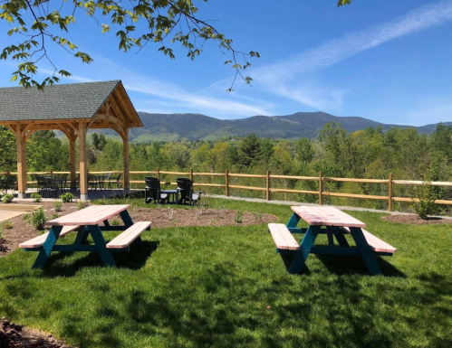 A scenic outdoor area with picnic tables, a gazebo, and mountains in the background under a clear blue sky.