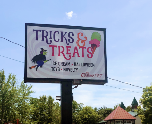 Sign for "Tricks & Treats" featuring ice cream, Halloween toys, and novelty items, with a witch and ice cream graphic.
