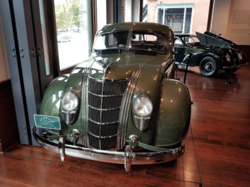 A vintage green car displayed indoors, showcasing its classic design and shiny chrome details.