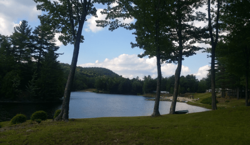 A serene lake surrounded by trees and hills, with a clear blue sky and a few people in the distance.