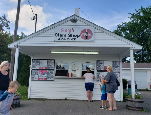 A small clam shop with a sign, featuring customers ordering at the window on a sunny day.