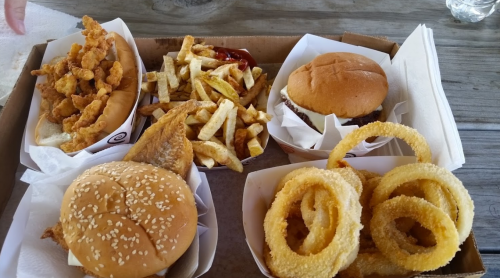 A tray of fast food featuring shrimp, fries, a burger, two sandwiches, and onion rings.