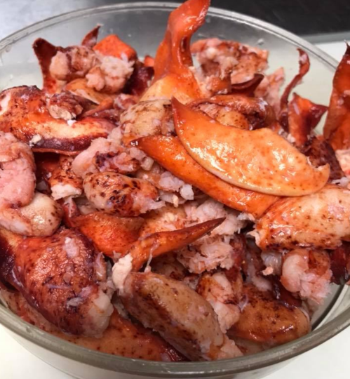 A bowl filled with cooked lobster meat and lobster claws, showcasing a rich, reddish-orange color.