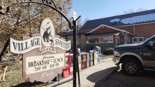 Sign for Village Smithy Restaurant, with outdoor seating and a truck parked nearby on a sunny day.