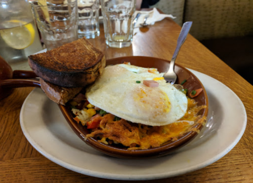 A dish with two fried eggs on top of a colorful hash, served with two slices of toasted bread on the side.