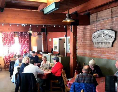 A cozy restaurant interior with wooden beams, red curtains, and diners at tables enjoying their meals.