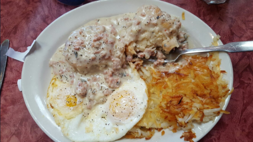 A plate of breakfast featuring two fried eggs, biscuits with sausage gravy, and crispy hash browns.