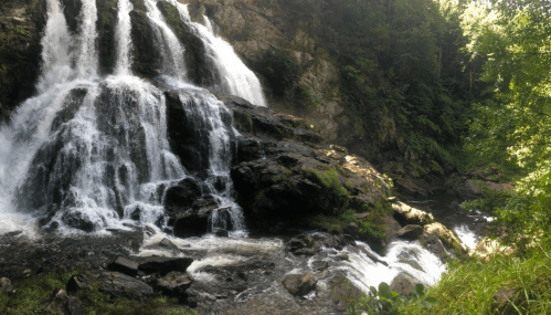 A serene waterfall cascading over rocky terrain, surrounded by lush greenery and sunlight filtering through the trees.