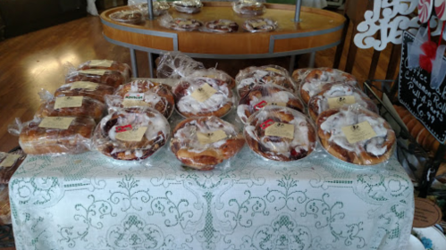 A display of assorted baked goods in clear packaging on a lace tablecloth, with labels on each item.