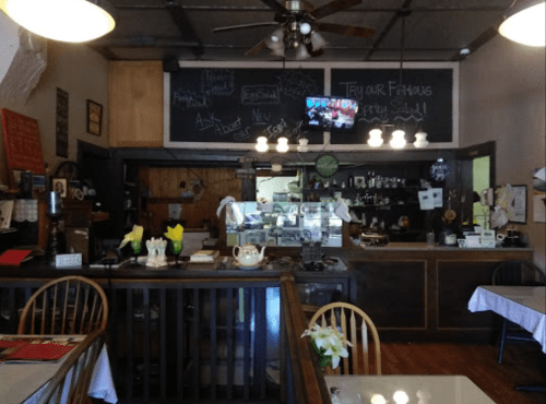 Cozy café interior with wooden furniture, a counter display, chalkboard menus, and a TV showing a program.