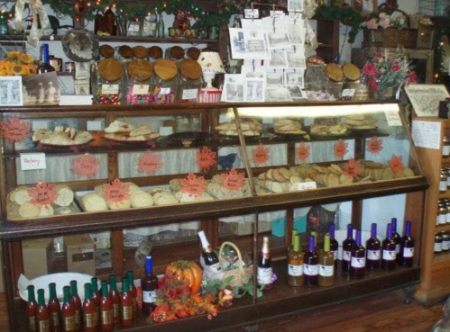 A display case filled with various baked goods and bottles of wine, decorated for the season with autumn leaves.