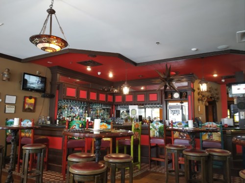 A cozy bar interior with red walls, wooden furniture, and a well-stocked counter, featuring decorative lighting.