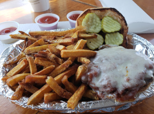 A plate of fries with a cheeseburger topped with pickles, served with three cups of ketchup on the side.