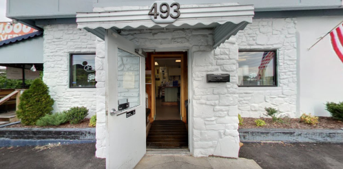 Entrance of a building with a white stone exterior, featuring an open door and the number 493 above it.