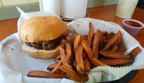 A burger with melted cheese on a bun, served with a side of crispy French fries and a small cup of ketchup.