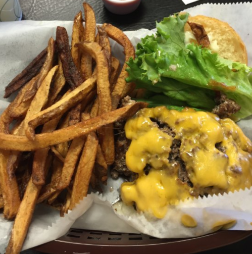 A plate with a cheeseburger topped with melted cheese, lettuce, and a side of crispy French fries.